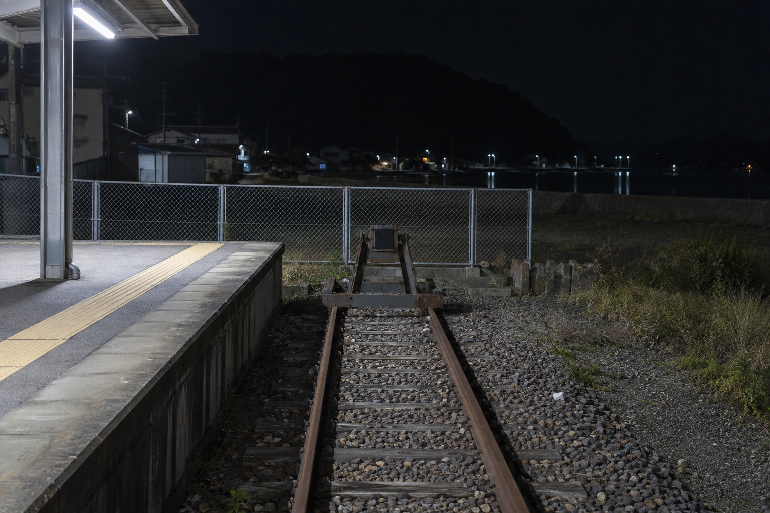 霧島秀一撮影。夜の汐見浜駅。ホームの先に車止めがあり、その奥に柵が立っている。