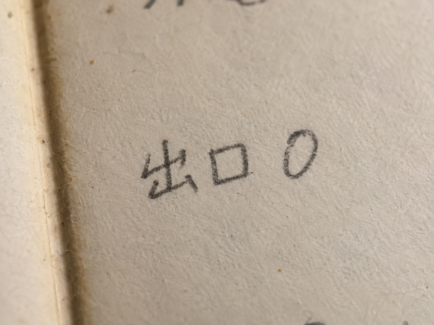 元担当者提供の手帳写真。少し黄ばんだ紙に、鉛筆で出口と数字の0が横に並べて書かれている。前後の記載は画面の端で切れている。