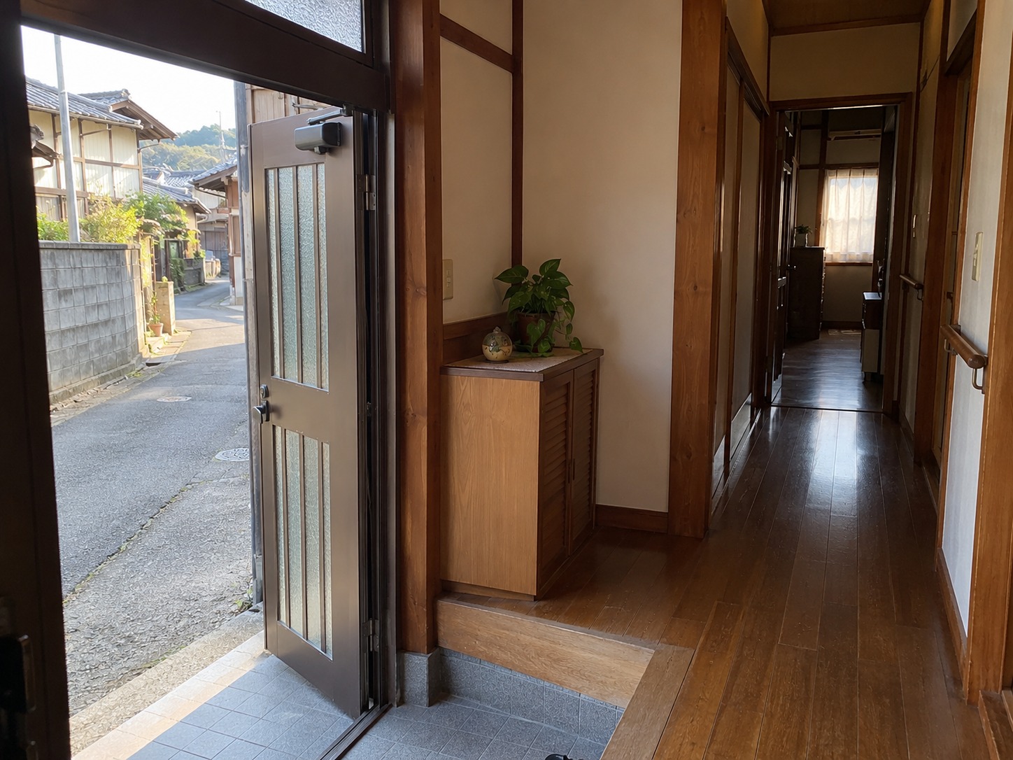 霧島秀一撮影。開いた玄関の戸の向こうに住宅街の道が見える。戸の脇には上がり口があり、木の廊下が家の奥へ続いている。