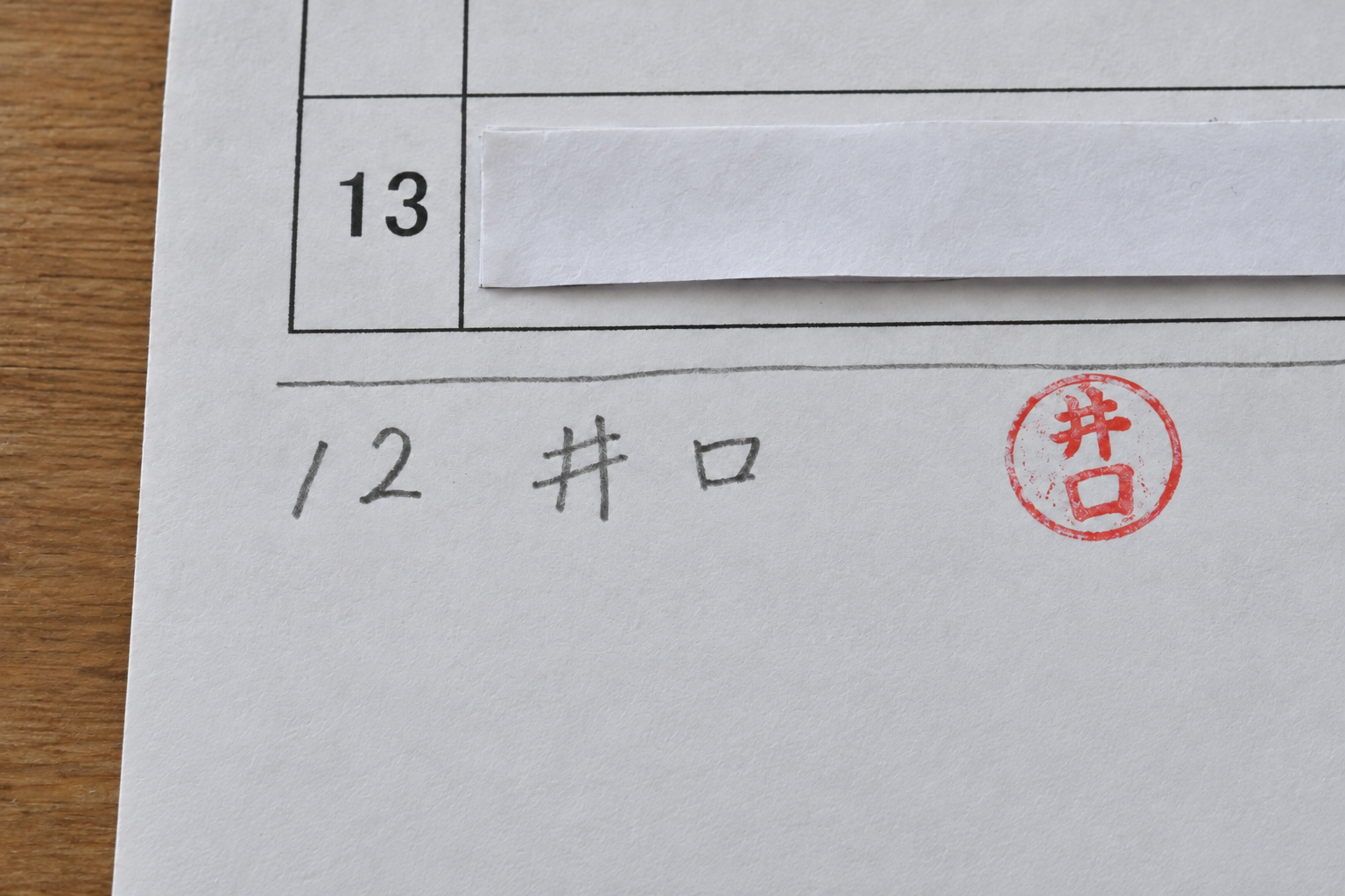 霧島秀一が撮影した4月の確認表の一部。印刷された13番の欄の下に、鉛筆で「12 井口」と書かれ、赤い丸い印が押されている。13番の住人の名前と印は白い紙で隠されている。
