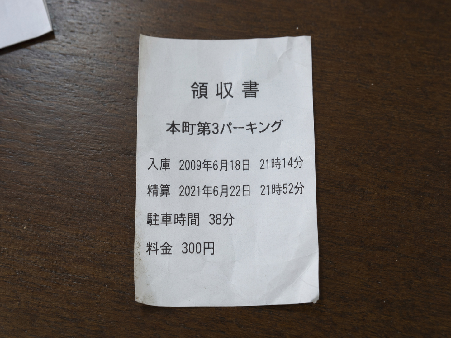 霧島秀一撮影。本町第3パーキングの領収書。入庫は2009年6月18日21時14分、精算は2021年6月22日21時52分と印刷されている。駐車時間は38分、料金は300円。