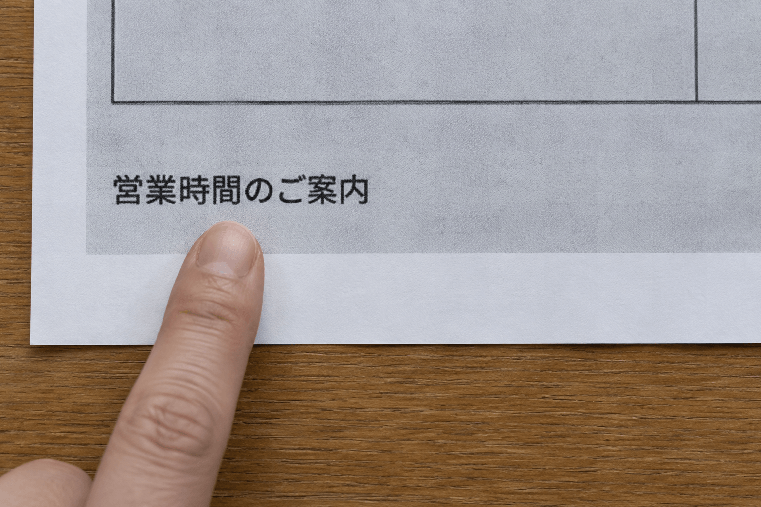 霧島秀一撮影。時刻表の写真を印刷した紙の下部。「営業時間のご案内」の文字の下を、森本さんの指が示している。