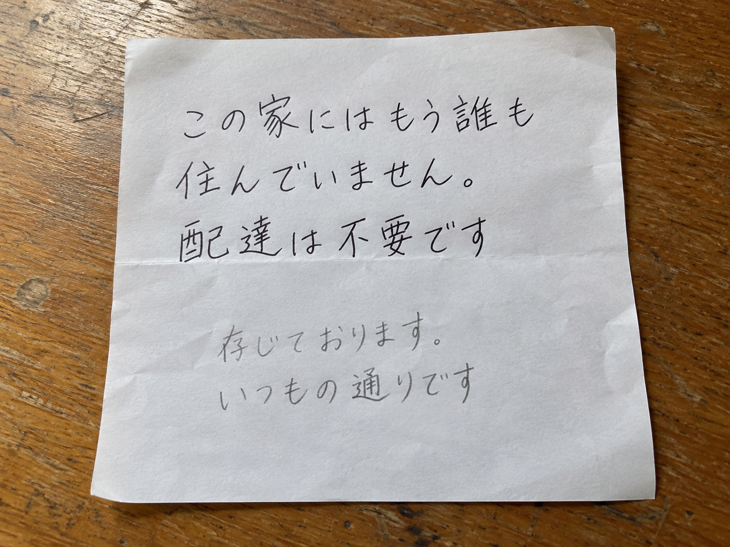 霧島秀一撮影。白い紙の上半分に「この家にはもう誰も住んでいません。配達は不要です」。下には薄い鉛筆で「存じております。いつもの通りです」と書き足されている。