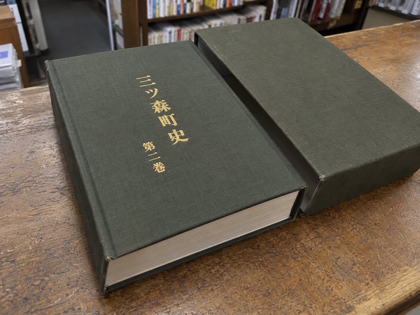 霧島秀一撮影。三ツ森書店に届いた本と箱。くすんだ緑色の布張りの表紙に、金色で「三ツ森町史」「第二巻」と縦書きされている。