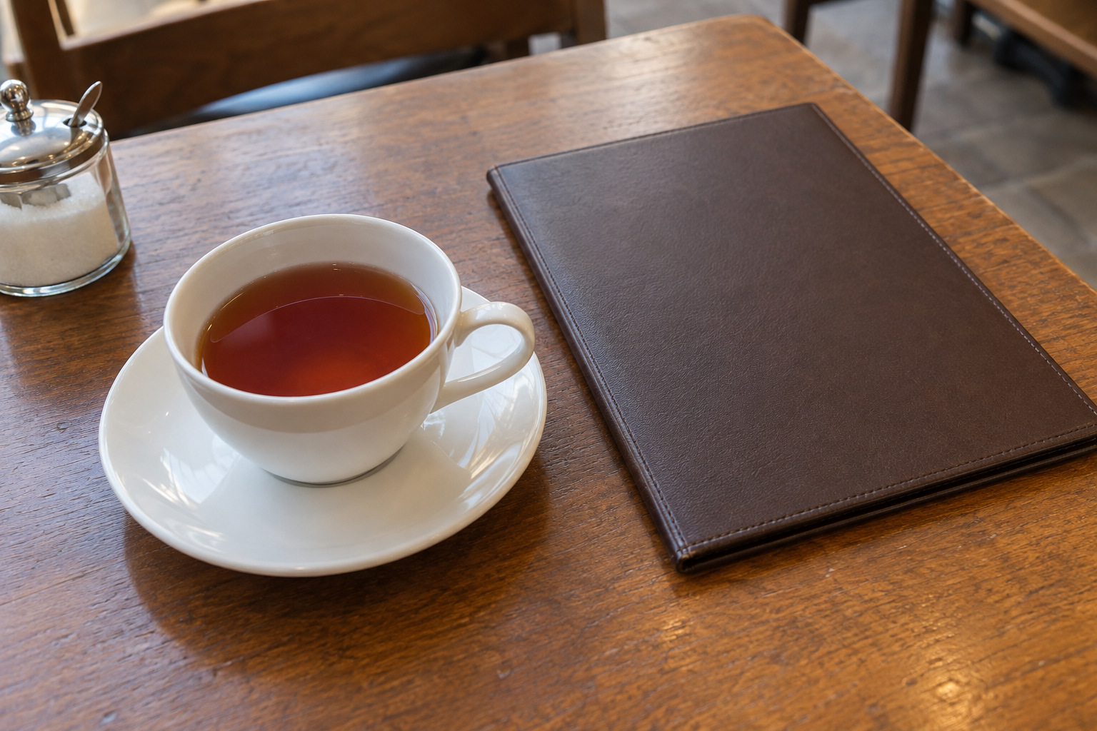 霧島秀一撮影。木の卓に置かれた白いカップと受け皿、閉じた濃茶色の品書き。カップには紅茶が半分ほど残っている。