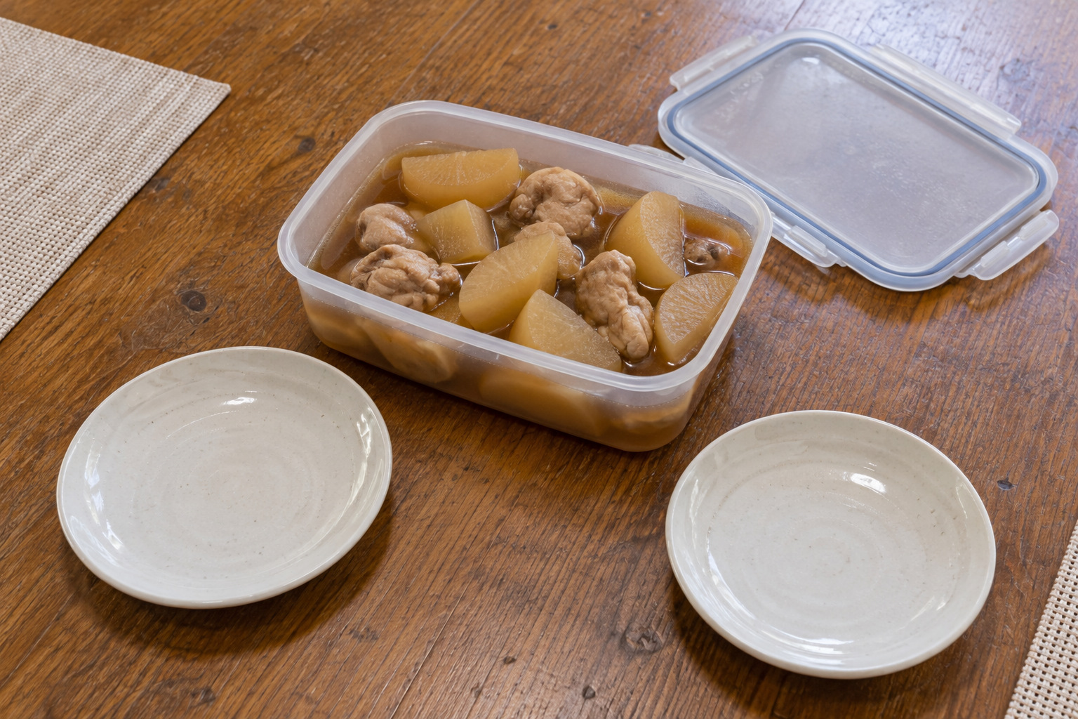 霧島秀一撮影。木製の食卓の上に、開いた角形の保存容器がある。中には大根と鶏肉の煮物が入り、脇には空の取り皿が2枚置かれている。