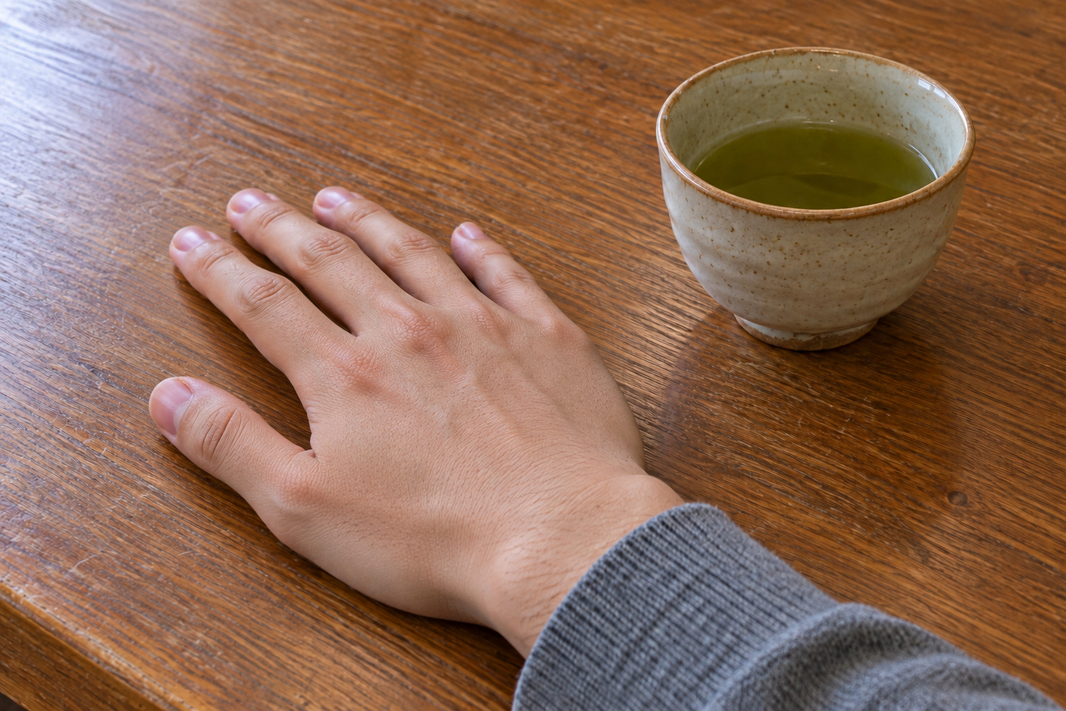 木の卓に伏せて置かれた成人男性の右手と、その脇の湯飲み。手の甲に深いしわは見えない。霧島秀一撮影。